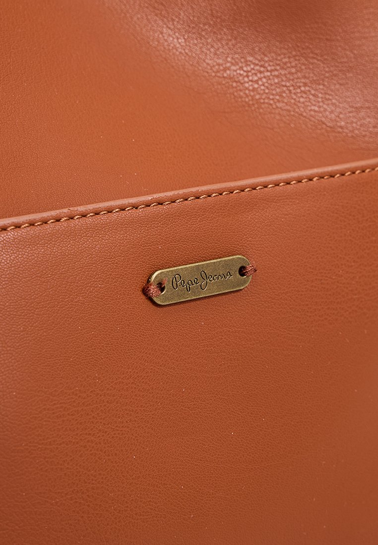Bolso de piel marrón claro con una pequeña etiqueta en tono dorado con el texto "Pepe Jeans", costuras delineadas y una textura suave.