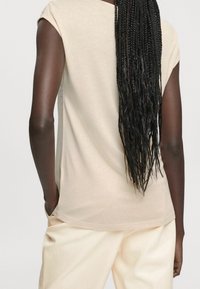 Béžový top s krátkým rukávem, zaobleným výstřihem, hladkou texturou a uvolněným střihem, doplněný o světlé kalhoty.