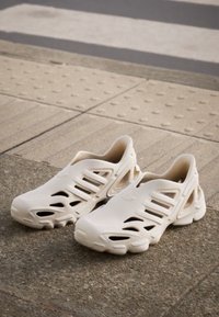 White slip-on shoes with cut-out design and textured upper, featuring a thick sole and ventilated accents for breathability.