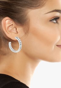 Silverhänge med en texturerad design och klara ädelstenar längs kanten, vilket skapar en glittrande accent. Lätta och cirkulära i formen.