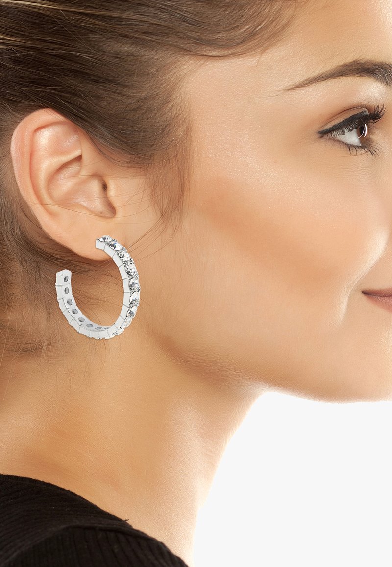 Silverhänge med en texturerad design och klara ädelstenar längs kanten, vilket skapar en glittrande accent. Lätta och cirkulära i formen.