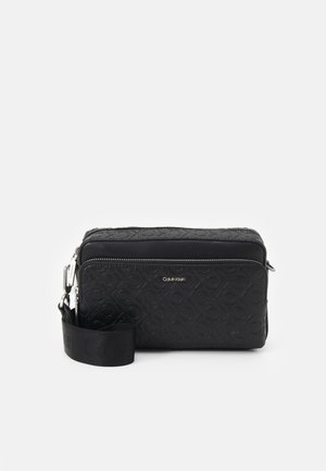 Zwarte rechthoekige crossbodytas van Calvin Klein met reliëf logo patroon, voorvak met ritssluiting en verstelbare stoffen schouderriem.