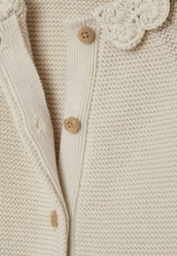 Strickjacke in Creme mit Holzknöpfen, ausgestattet mit einem strukturierten Muster und einem gewellten Kragen.