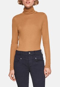 Hauts à manches longues en turtleneck de couleur beige fabriqué dans un tissu doux, avec un design ajusté et un col haut. Associé à un jean bleu marine foncé.