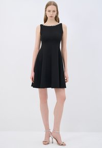 Vestido negro sin mangas con un corsé ajustado y falda acampanada. Presenta un escote adornado con joyas y está hecho de una tela suave.