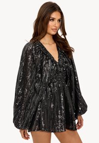 Combinaison à paillettes noires avec un décolleté en V profond, tissu texturé et manches larges. Présente des rayures verticales et un perlage complexe autour du col.