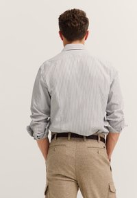 Camicia a maniche lunghe con strisce verticali blu e bianche, in tessuto di cotone, con polsini a bottoni. Abbinata a pantaloni cargo color khaki, con due tasche posteriori e una cintura.