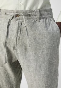 Light gray linen trousers with an elastic waistband, drawstring closure, and side pockets. Textured fabric with a natural finish.