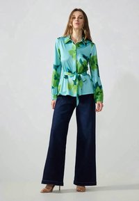 Long-sleeve button-up shirt in blue and green watercolor print, paired with wide-leg dark denim pants and beige heels.
