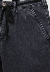 Tmavě modré džínové kalhoty s šňůrkovým pasem, dvěma předními kapsami a texturovaným povrchem s jemnými detaily šití.