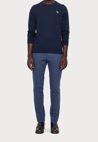 Marinblå tröja med ribbade ärmslut och krage, prydd med en liten logotyp. Ljust blå slim-fit-byxor, tillsammans med blanka mörka skor.