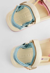 Bequeme, geschlossene Sandalen mit Riemen in Blau und Beige, ausgestattet mit einer strukturierten, wellenförmigen Laufsohle und einem eingeprägten Logo auf dem Fußbett.