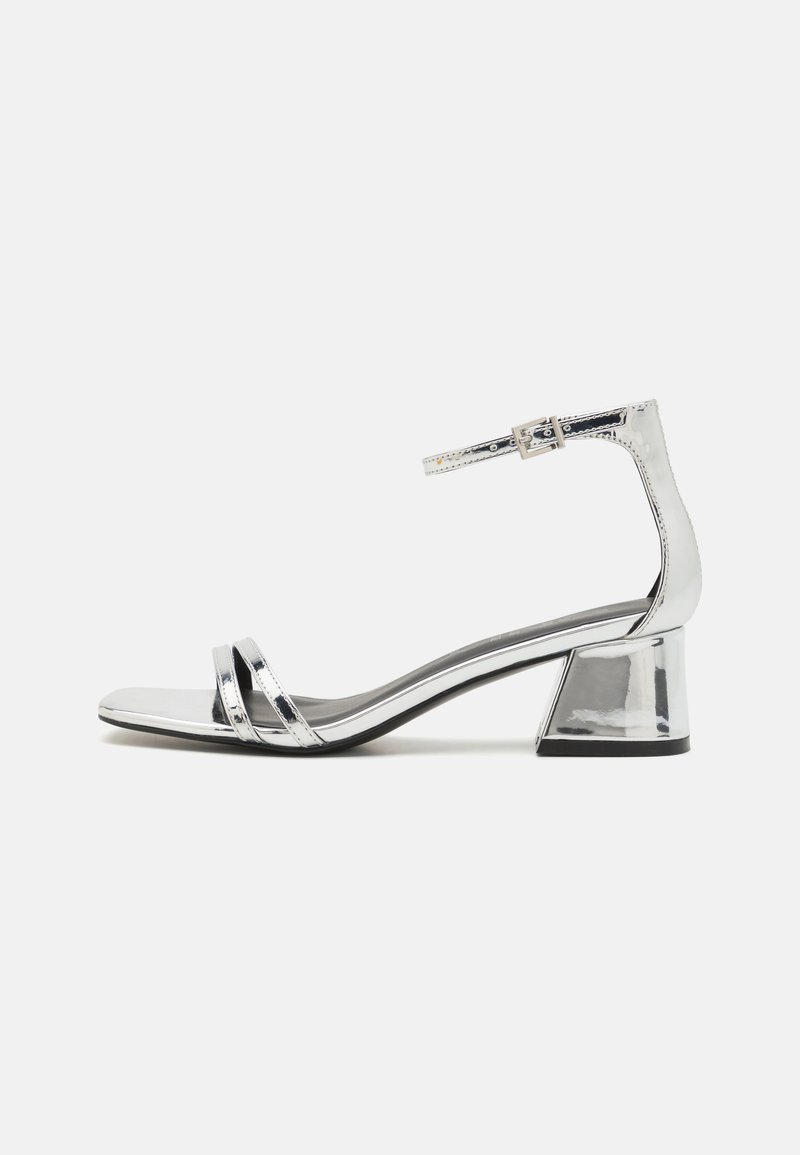 Sandali con tacco argento caratterizzati da una finitura lucida, due cinturini frontali, cinturino alla caviglia con fibbia e un tacco a blocco. Progettati con una silhouette elegante.