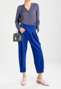 Blusa a righe navy, pantaloni azzurri a vita alta, borsa a tracolla verde e scarpe chiare con lacci rosa. I pantaloni hanno le maniche ripiegate.