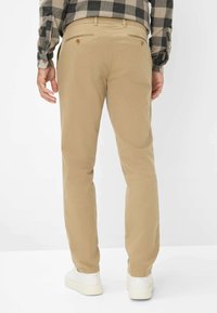 Beige Chinos mit Slim Fit. Sie verfügen über zwei Gesäßtaschen mit Knöpfen, Knöchelbündchen und eine glatte Textur. Tragen Sie sie mit weißen Sneakers.