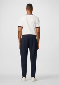 Witte korte mouwen shirt met bordeaux trim, gecombineerd met marineblauwe joggingsbroek. Witte sneakers maken de outfit compleet. Eenvoudig ontwerp, casual pasvorm.