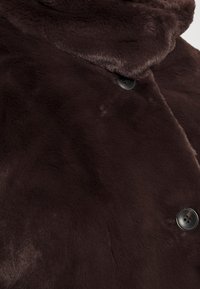 Bruine imitatiewollen jas met een zachte textuur, voorzien van een hoge kraag en een enkele knoopsluiting voor extra functionaliteit.