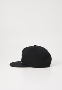 Black baseball cap with a flat brim, made of fabric, featuring white embroidered detailing on the front and ventilation holes on the sides.