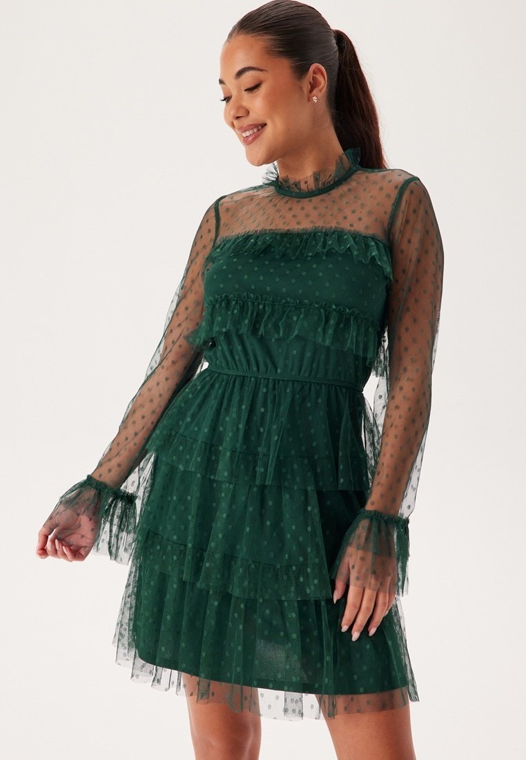 Robe verte à volants en tissu transparent avec des pois, dotée de longues manches transparentes, de volants et d'une taille cintrée.