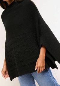 Poncho lavorato a maglia nero con collo alto, caratterizzato da un motivo a treccia testurizzato al centro e maniche larghe e fluenti.