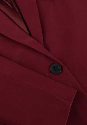 Burgundy blazer featuring a notch lapel, single black button closure, and fine texture. Detail of tailored stitching is visible.