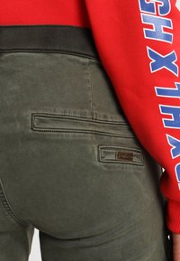Mörkgröna byxor med detaljer på bakfickan, med en texturerad yta och en liten metalltagg "ONLY". Röd sweatshirt med blå bokstäver.
