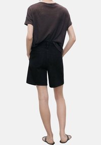 Shorts de mezclilla negra con un corte clásico, talle medio y bolsillos traseros. Combinados con una camiseta oscura de corte holgado y sandalias planas.