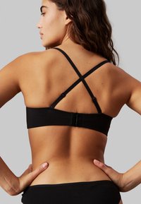 Reggiseno nero con spalline incrociabili regolabili. Tessuto liscio, fascia ampia e chiusura a gancio sul retro. Linee pulite e design minimale.