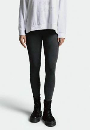 Schwarze, strukturierte Sportleggins kombiniert mit einem weißen Sweatshirt, ergänzt durch schwarze Schnürstiefel mit dicken Sohlen.