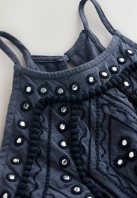 Haut sans manches bleu marine avec fines bretelles, tissu texturé et clous argentés circulaires disposés en motifs sur le devant.