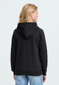 Svart hettegenser med snøring, lange ermer og en avslappet passform. Har ribbestrikkede mansjetter og hem, laget av myk, teksturert stoff.