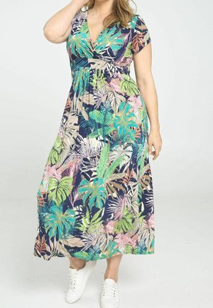 Maxikleid in Marineblau mit einem tropischen Blattmuster in Grün-, Pink- und Weißtönen. Kurze Ärmel und ein Wickeldesign, kombiniert mit weißen Turnschuhen.