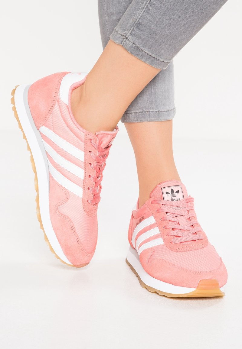 Rosa sportskor i mocka och mesh-material, med vita ränder, en strukturerad gummisula och en signaturlogotyp på tungan.