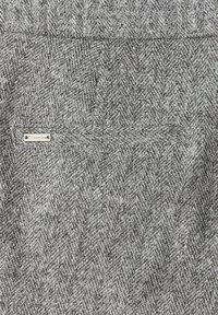 Szary materiał w jodełkę z delikatną teksturą. Zawiera małą metalową metkę wszytą w szew, wskazującą markę.