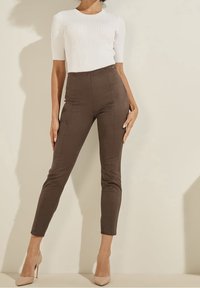 Pantalons taille haute marron avec une texture douce et un design ajusté. Associés à un haut blanc à manches courtes côtelé et des talons hauts nude.