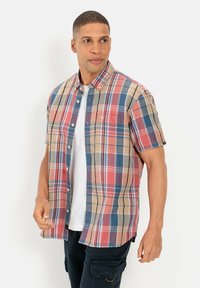 Korte mouwen geruite shirt in beige, rood en blauw. Voorzien van een knoopsluiting kraag en een borstzak. Draagt over een witte T-shirt.