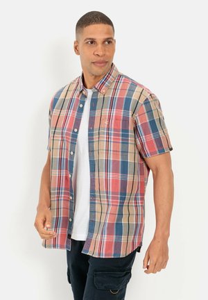 Kurzarm-Hemden aus Karo in Beige, Rot und Blau. Mit einem knöpfbaren Kragen und einer Brusttasche. Über einem weißen T-Shirt getragen.
