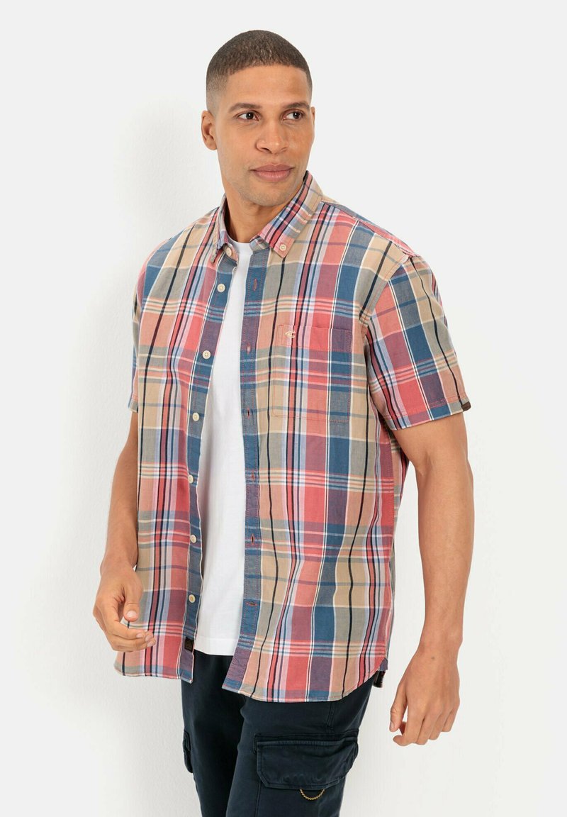Korte mouwen geruite shirt in beige, rood en blauw. Voorzien van een knoopsluiting kraag en een borstzak. Draagt over een witte T-shirt.