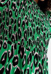 Vestido verde con un cuerpo fruncido, que presenta un patrón de leopardo negro y rosa. Mangas cortas con volantes y un diseño de falda fluida.