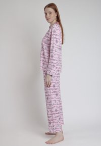 Juego de pijama rosa que incluye una camiseta de manga larga y pantalones a juego, con un patrón divertido de personajes de dibujos animados y texto en contornos negros.