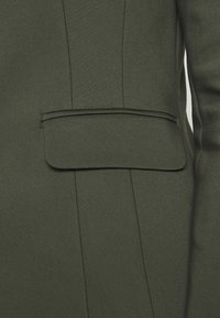Dark green tailored blazer featuring a clean silhouette, a side pocket, and textured fabric with a smooth finish and subtle seams.