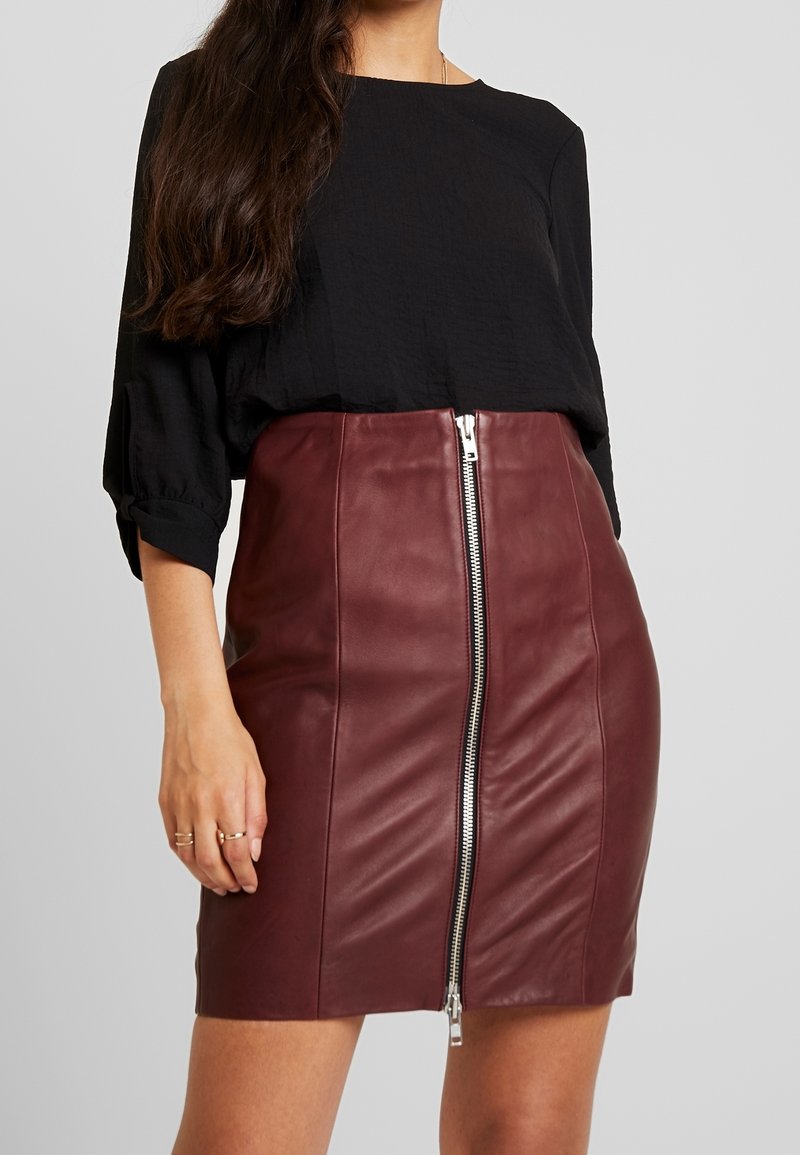 Blusa nera in tessuto testurizzato con maniche a tre quarti abbinata a una gonna in pelle bordeaux aderente con dettaglio della cerniera argentata.