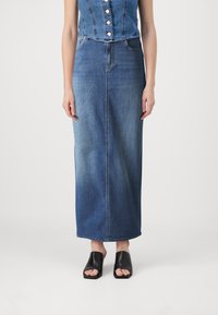 Denim maksi krilo v srednje modri barvi s ravnim krojem, ki ima sprednji šiv, nosi pa se z črnimi odprtimi mule čevlji. Tekstura je gladka.