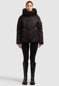 Black puffer jacket with a high collar, featuring a geometric quilted design and a fitted shape. Paired with black leggings and knee-high boots.