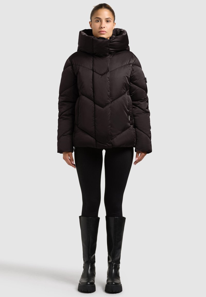 Black puffer jacket with a high collar, featuring a geometric quilted design and a fitted shape. Paired with black leggings and knee-high boots.