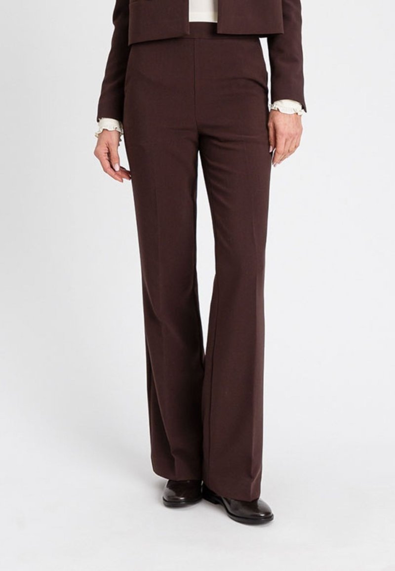 Pantaloni marroni su misura con un design a gamba svasata, texture liscia e vita media, abbinati a un giubbotto aderente e un top crema.