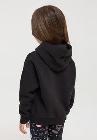 Czarna bluza z kapturem, z prążkowanymi mankietami i dołem. Tył ma prosty, minimalistyczny design bez widocznych logotypów czy wzorów.