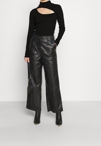 Svart långärmad topp med ett utskärningsdetalj, kombinerad med höga svarta läderbyxor med vida ben och spetsiga anklarstövlar.