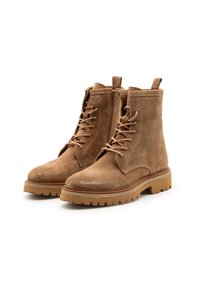 Botas de tobillo de ante marrón con cordones en la parte frontal, acabado de textura suave y suelas de goma beige con patrón de relieve para mayor tracción. Detalle de cremallera lateral.