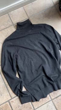 Maglione collo alto grigio scuro realizzato in morbido tessuto a maglia testurizzato. Presenta maniche lunghe e un orlo a coste aderente.